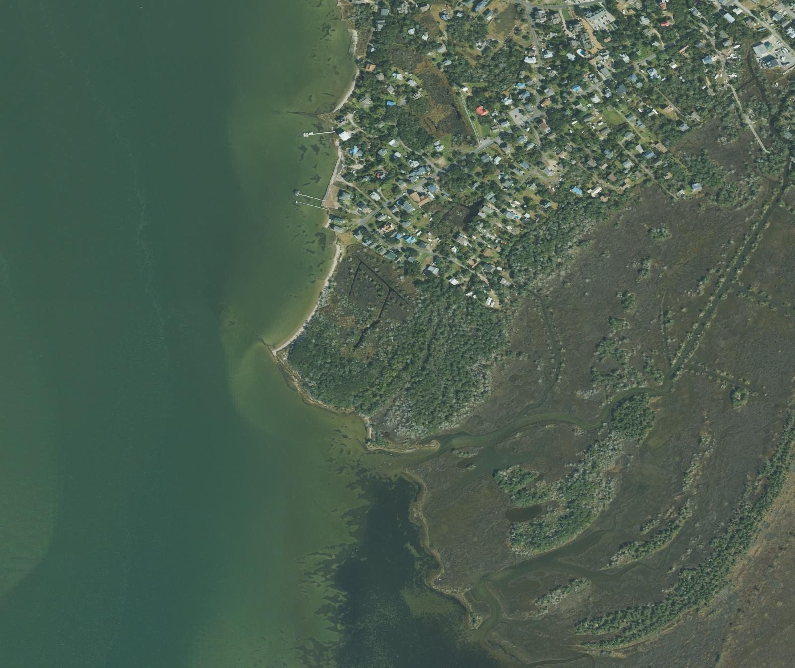 Aerial photograph of the south end of Ocracoke village showing where the houses stop and the wooded Springer's Point Preserve begins, with Pamlico Sound to the west